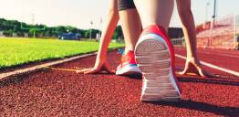 Je ziet de voeten van een hardloper die op het punt staat te starten op een atletiekbaan. De hardloper draagt sportschoenen.