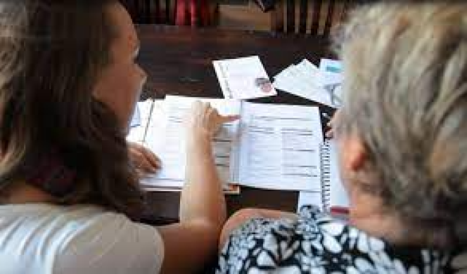 foto van twee mensen waarvan de een de ander helpt met de administratie