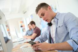 jongen achter pc kijkt op mobiele telefoon