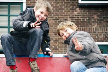 Decoratieve afbeelding: Twee jongens op de basisschool zijn buiten en lachen naar de camera met hun vingers in de lucht